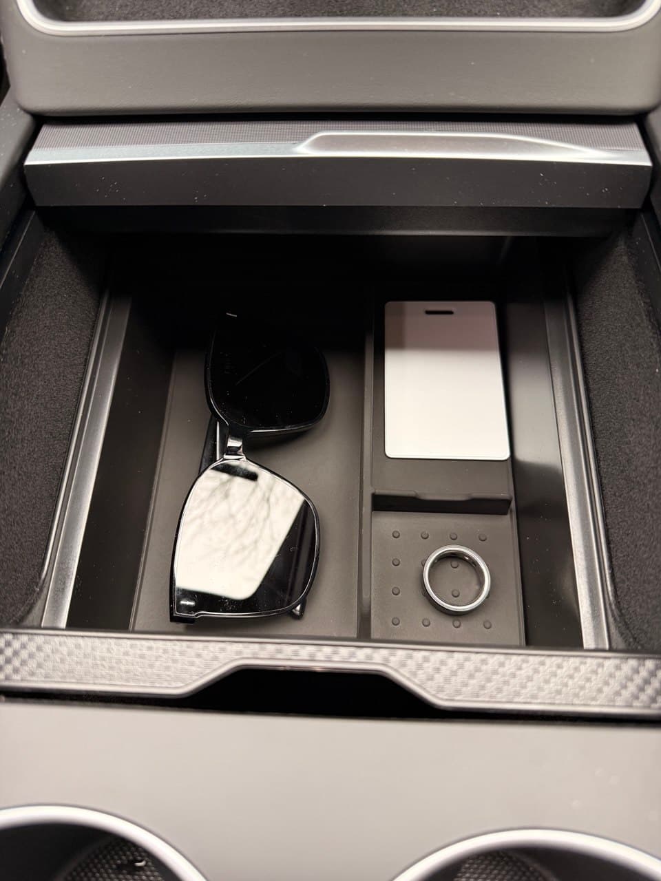 Console storage box holding sunglasses, cards, and a ring