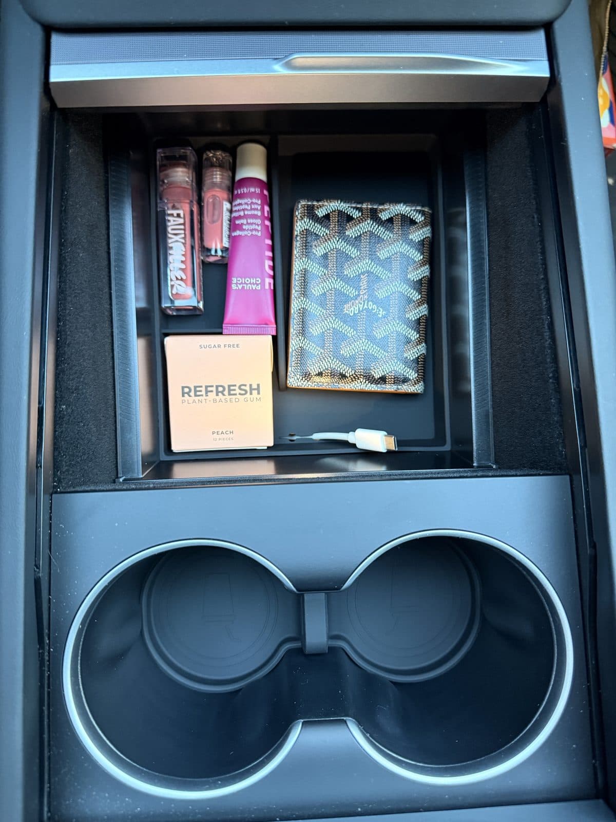 SUMK front tray installed in Tesla Model Y Juniper holding lip products, a wallet and a small box with a cable routed through